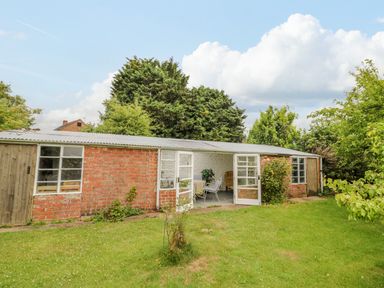 A brick outbuilding with open glass doors and garden furniture on a lawn at Priors Mead in Claydon near Cropredy
