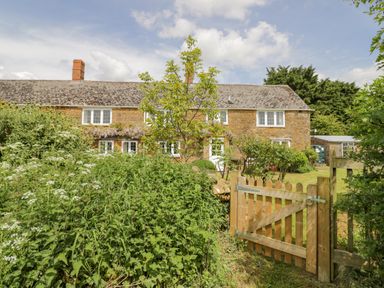 A garden with plants and a wooden gate in front of a stone house at Priors Mead in Claydon near Cropredy