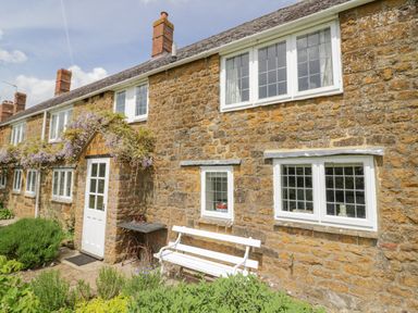 Stone cottage exterior with white door bench and flowering plants at Priors Mead Claydon near Cropredy