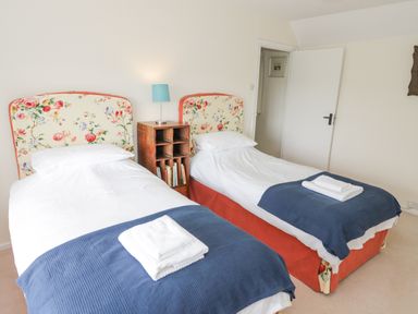 A bedroom with two single beds with floral headboards blue throws and a wooden nightstand with a lamp at Priors Mead in Claydon near Cropredy