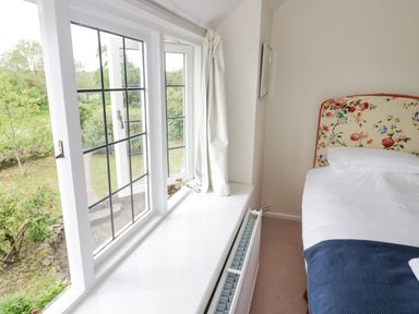 A bedroom with a floral headboard bed next to a window with white frames and curtains at Priors Mead Claydon near Cropredy