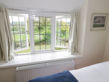A bedroom with an open window overlooking greenery and white curtains at Priors Mead Claydon near Cropredy