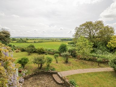 A garden with shrubs and trees overlooking fields and countryside at Priors Mead Claydon near Cropredy