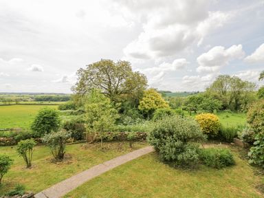 A garden with bushes trees and a stone wall overlooking fields at Priors Mead Claydon near Cropredy