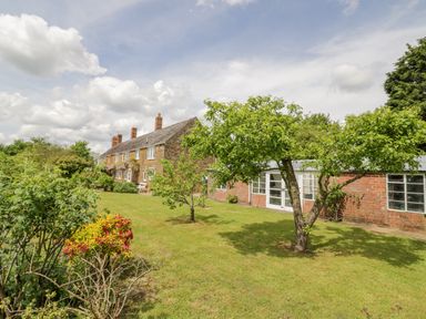 A garden with trees and bushes beside a row of brick houses at Priors Mead in Claydon near Cropredy