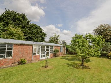 A garden with grass trees and a brick outbuilding with windows and a door at Priors Mead in Claydon near Cropredy