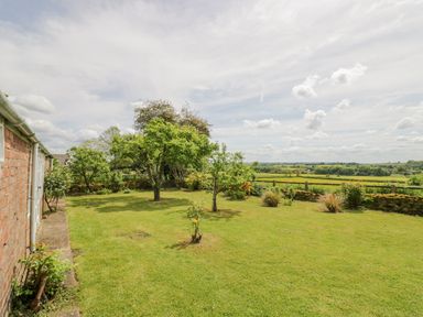A garden with trees grass and a stone wall with countryside view at Priors Mead in Claydon near Cropredy