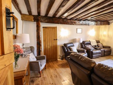 A living room with leather sofas armchair wooden beams and a door at Cwm Yr Afon Mawr in Llanbedr near Harlech