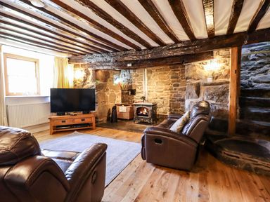 A living room with leather armchairs a wood burning stove stone walls television and wooden ceiling beams at Cwm Yr Afon Mawr in Llanbedr near Harlech