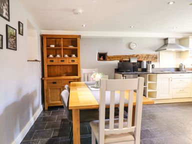 A kitchen with wooden dining table and chairs a wooden cabinet and kitchen appliances at Cwm Yr Afon Mawr in Llanbedr near Harlech