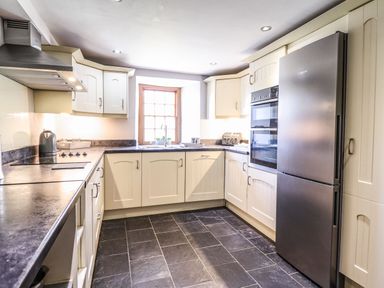 A kitchen with white cabinets black countertops a stainless steel refrigerator and oven and a window above the sink at Cwm Yr Afon Mawr Llanbedr near Harlech