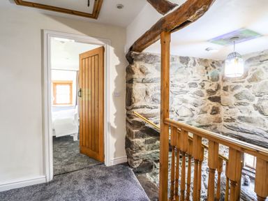 A hallway with a wooden door leading to a bedroom and a staircase with wooden railing and stone walls at Cwm Yr Afon Mawr in Llanbedr near Harlech