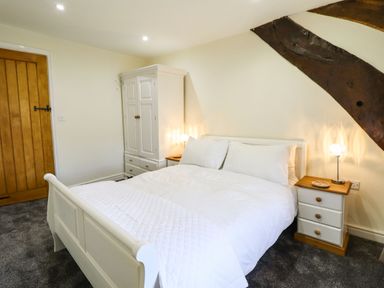A bedroom with a white bed white wardrobe white bedside tables and wooden beams at Cwm Yr Afon Mawr in Llanbedr near Harlech
