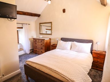 A bedroom with a bed, two wooden bedside tables, a wooden dresser with a mirror above and a wall-mounted TV at Cwm Yr Afon Mawr in Llanbedr near Harlech