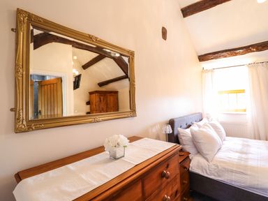 A bedroom with a wooden dresser and mirror next to a bed with pillows and a window with curtains at Cwm Yr Afon Mawr in Llanbedr near Harlech