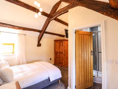 A bedroom with exposed wooden beams a bed a wooden wardrobe and an open door leading to a bathroom at Cwm Yr Afon Mawr in Llanbedr near Harlech