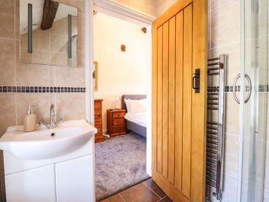 A bathroom with a sink and mirror looking into a bedroom with a bed and wooden nightstand at Cwm Yr Afon Mawr in Llanbedr near Harlech