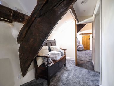 A hallway with a dark wooden bench with cushions and folded towels under exposed wooden beams at Cwm Yr Afon Mawr in Llanbedr near Harlech