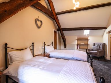 A bedroom with two single beds a gray armchair and wooden beams on the ceiling at Cwm Yr Afon Mawr in Llanbedr near Harlech