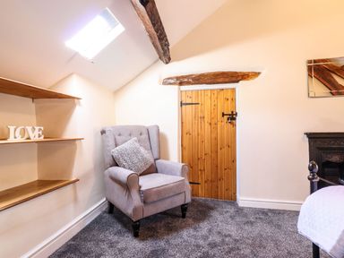 A gray armchair with a pillow near wooden door and shelves with love decoration at Cwm Yr Afon Mawr in Llanbedr near Harlech