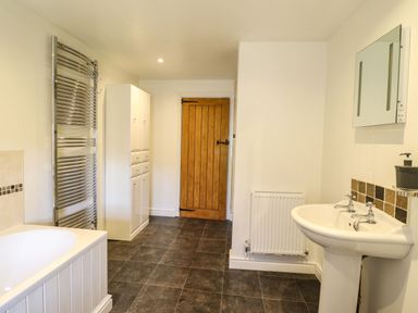 A bathroom with a bathtub radiator cabinet wooden door sink and mirror at Cwm Yr Afon Mawr Llanbedr near Harlech