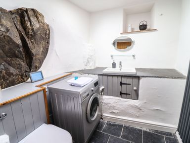 A bathroom with a washing machine a sink an oval mirror and exposed rock wall at Cwm Yr Afon Mawr Llanbedr near Harlech