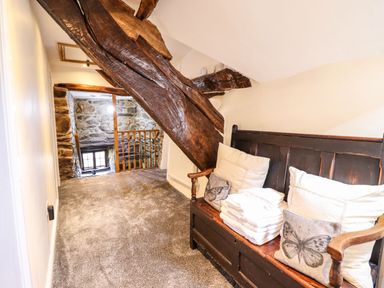 A hallway with wooden beams a bench with pillows and folded towels and a stone wall at Cwm Yr Afon Mawr in Llanbedr near Harlech