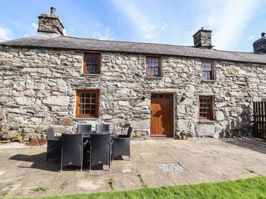 An outdoor patio with a table and chairs in front of a stone building at Cwm Yr Afon Mawr in Llanbedr near Harlech