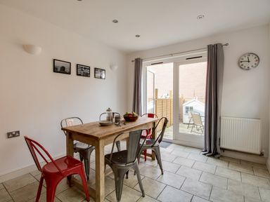 A dining area with a wooden table and metal chairs next to glass doors with grey curtains at Sandsfoot Rest in Weymouth