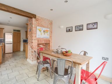 A dining area with a wooden table and metal chairs next to a brick fireplace and kitchen at Sandsfoot Rest in Weymouth