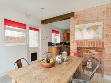 A dining area with a wooden table metal chairs a bowl of fruit and a map on a brick wall at Sandsfoot Rest in Weymouth