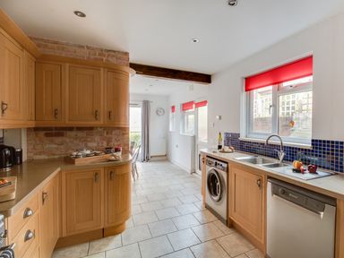 A kitchen with wooden cabinets a washing machine dishwasher and red window blinds at Sandsfoot Rest in Weymouth