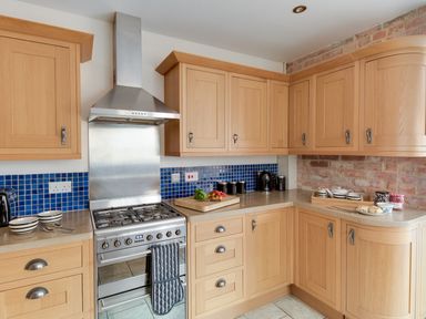 A kitchen with wooden cabinets a stainless steel oven and stove a blue tiled backsplash and a cutting board with vegetables at Sandsfoot Rest in Weymouth