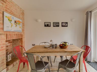 A dining area with a wooden table and metal chairs next to a brick fireplace with a world map at Sandsfoot Rest in Weymouth