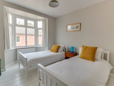 A bedroom with two single beds a wooden nightstand with a blue lamp and a framed picture on the wall at Sandsfoot Rest in Weymouth