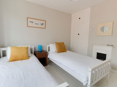 A bedroom with two single beds with yellow pillows and a small wooden nightstand with a blue lamp between them at Sandsfoot Rest in Weymouth