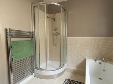 A bathroom with a corner shower enclosure a towel rack with a green towel and a bathtub at Sandsfoot Rest in Weymouth