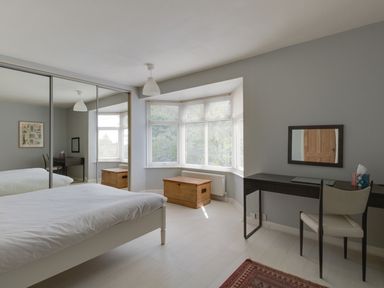 A bedroom with a bed a desk and chair a wooden chest under a window and mirrored sliding closet doors at Sandsfoot Rest in Weymouth