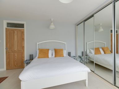 A bedroom with a white bed with orange pillows a wooden door and mirrored sliding wardrobe doors at Sandsfoot Rest in Weymouth