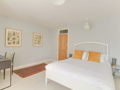 A bedroom with a white bed with orange pillows a wooden door a rug two framed pictures and a desk with a chair at Sandsfoot Rest in Weymouth