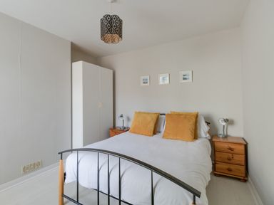 A bedroom with a double bed with mustard pillows a wardrobe two wooden bedside tables and three pictures on the wall at Sandsfoot Rest in Weymouth