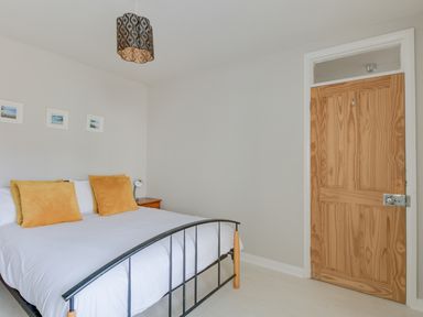 A bedroom with a bed with white bedding and orange pillows next to a wooden door at Sandsfoot Rest in Weymouth
