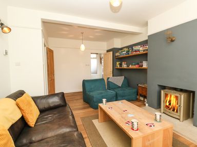 A living room with a brown leather sofa two blue chairs a wooden coffee table with mugs and cards a fireplace and shelves with board games at Sandsfoot Rest in Weymouth