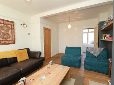 A living room with a brown leather sofa two blue chairs a wooden coffee table and shelves with board games at Sandsfoot Rest in Weymouth