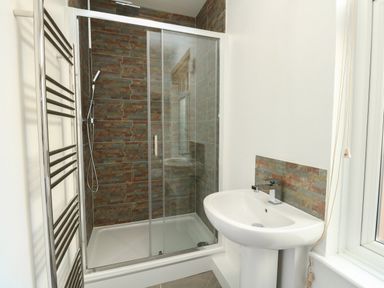 A bathroom with a glass shower enclosure a tiled wall a white sink and a metal towel rack at Sandsfoot Rest in Weymouth