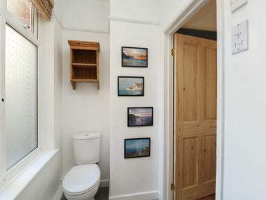 A bathroom with a toilet wooden shelf and framed pictures on the wall at Sandsfoot Rest in Weymouth