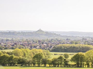 A landscape with trees green fields houses and a hill with a tower in the distance at Foxglove in Sticklinch West Pennard Glastonbury