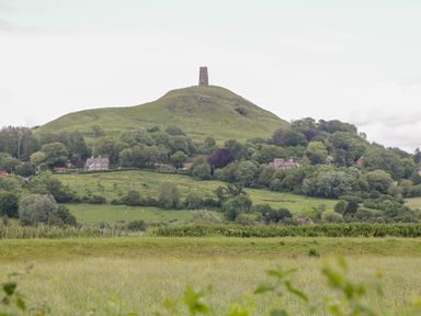 A hill with a tower on top surrounded by trees and houses in a green landscape at Foxglove in Sticklinch West Pennard Glastonbury