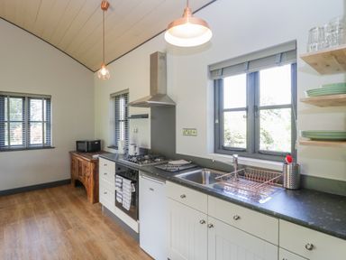 A kitchen with white cabinets a gas stove a sink and wooden shelves at Foxglove in Sticklinch West Pennard Glastonbury