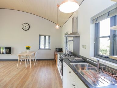 A kitchen with a dining table with flowers a wall clock and a sink with a dish rack at Foxglove in Sticklinch West Pennard Glastonbury